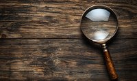 Vintage magnifying glass with wooden handle lying on rustic wooden table background, dramatic lighting creates mysterious detective atmosphere.