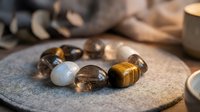 Healing crystal bracelet with tiger eye and moonstone beads on natural stone surface with candles creating peaceful meditation atmosphere for wellness.
