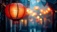 Traditional red paper lantern glowing against blurred evening street with warm bokeh lights creating atmospheric festive mood for celebration design.