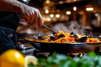 Traditional Spanish seafood paella with mussels and shrimp being served in cast iron pan, steam rising over vibrant saffron rice, restaurant atmosphere with bokeh lights.