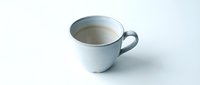 Simple white ceramic coffee mug with light brown coffee on clean white background. Minimalist kitchen tableware isolated for design projects.