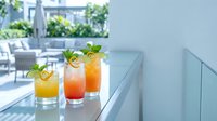 Three colorful layered cocktails with fresh mint garnish on modern outdoor terrace bar counter, summer refreshing drinks for hospitality and beverage service.