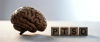 Wooden brain model beside letter blocks spelling PTSD on a neutral surface, symbolizing post-traumatic stress disorder awareness and mental health education.