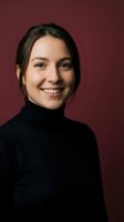 Young Caucasian woman in black turtleneck smiling warmly at camera against burgundy background for professional headshot and business portrait use.