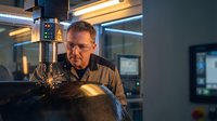 Skilled middle-aged Caucasian male welder working with precision equipment in modern industrial manufacturing facility with advanced machinery and lighting.