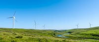 Wind turbines dotting rolling green hills with a small pond, representing renewable energy and sustainable power generation in rural landscape.