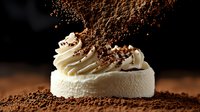 Creamy white meringue dessert topped with whipped cream swirl and falling cocoa powder on dark background, dramatic food photography for menu design.