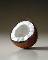 Fresh halved coconut showing white flesh and brown shell against neutral background, dramatic lighting creates depth and shadow on smooth surface.