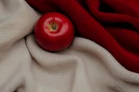 Fresh red apple on soft beige fabric with contrasting burgundy textile, creating elegant composition for food photography and lifestyle content.