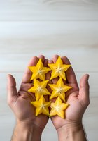 Hands holding fresh yellow star fruit slices arranged in pattern against white wooden background, suitable for food photography, healthy eating content, and culinary design projects.