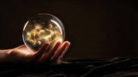 Hand holding glowing crystal ball with magical golden light and sparkles against dark background for fortune telling and mystical concepts.