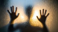 Silhouette of hands pressed against wet glass surface with water droplets and warm light creating dramatic shadow effect for emotional storytelling concepts.