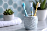 Colorful toothbrushes in ceramic holder on bathroom counter with white towel and succulent plant against hexagonal tile wall background. Modern dental care concept.