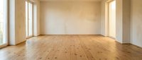 Empty room interior with wooden parquet flooring and white walls featuring large windows providing natural light for home renovation projects.
