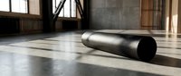 Black foam roller on concrete floor in modern industrial gym space for fitness recovery and muscle therapy exercises.