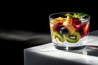 Fresh fruit cocktail with kiwi, raspberry, blueberry and mint in glass with ice cubes on dark background with dramatic lighting and copy space.