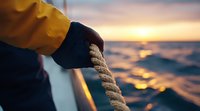 Close-up of sailor hands holding ship rope at golden sunset over ocean waves, dramatic maritime atmosphere with warm evening light reflections on water.