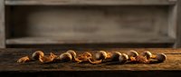 Roasted cashew nuts arranged in a row on rustic wooden surface with blurred wooden shelf background, suitable for food and culinary design projects.
