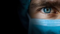 Close-up view of intense blue eye with medical face mask, dramatic lighting creates mysterious atmosphere. Healthcare and protection concept in dark setting.