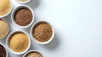 Assorted whole grains and seeds in white bowls on marble surface for healthy cooking and nutrition concepts.