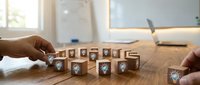 Business professional arranging wooden blocks spelling PRODUCTIVE with shield icons on office desk, symbolizing workplace efficiency and security management.