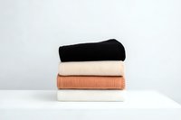 Stack of folded knitted sweaters in neutral colors black, beige, terracotta and white on white surface against light background. Minimalist fashion concept.