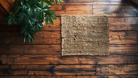 Natural burlap fabric on rustic wooden floor with green plant leaves in corner, perfect for product display background or eco-friendly design concept.