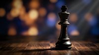 Black chess king piece standing alone on wooden board with blurred colorful bokeh lights background creating dramatic atmosphere for strategy and leadership concepts.