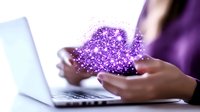 Young woman holding glowing purple digital particles between hands while working on laptop computer, representing digital transformation and innovation.