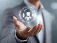 Asian businessman in gray suit holding glowing virtual customer service icon floating above palm, representing digital support and technology innovation in business.