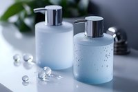 Frosted glass cosmetic bottles with silver pump dispensers on light background with water drops and glass beads, elegant bathroom accessories.
