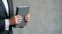 Man in business suit holding tablet device against gray background for corporate technology concepts.