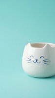 White ceramic cat-shaped mug with cute face on turquoise background for kitchen decor and beverage serving.