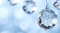 Crystal glass ornament with delicate snowflake pattern hanging against soft blue bokeh background, creating magical winter holiday atmosphere.