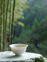 Steaming hot tea in ceramic bowl on stone surface with bamboo forest background creating peaceful zen atmosphere for meditation and relaxation.