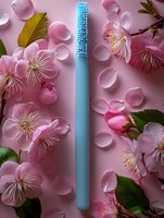 Blue silicone brush surrounded by delicate pink cherry blossoms and scattered petals on pink background, creating soft spring wellness composition.