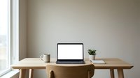 Minimalist home office workspace with open laptop, coffee mug and plant on wooden desk by window. Clean modern interior design for remote work productivity.