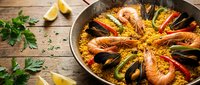 Traditional Spanish paella with seafood, saffron rice, mussels and prawns in authentic paellera pan on rustic wooden table with fresh herbs and lemon wedges.