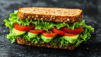 Fresh vegetarian sandwich with lettuce, tomato and avocado on multigrain bread served on dark slate surface for healthy eating and lunch concepts.