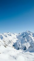Panoramic view of snow-covered alpine peaks under clear blue sky, showcasing majestic mountain range with pristine white slopes and rocky ridges. Ideal for travel, nature, and winter sports marketing materials.