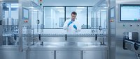 Male scientist in white lab coat working with laboratory equipment in modern sterile pharmaceutical manufacturing facility with stainless steel surfaces.