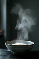 Steaming white rice in dark ceramic bowl against black background, rising vapor creates ethereal patterns in moody lighting, minimalist food photography.