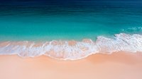 Aerial view of turquoise ocean waves gently rolling onto pristine sandy beach with white foam creating natural patterns along shoreline. Tranquil tropical seascape.