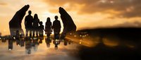 Business team silhouettes standing together during golden sunset reflecting on water surface creating powerful teamwork and leadership concept.