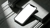 Modern smartphone with blank white screen lying on concrete surface with dramatic geometric shadows from window blinds creating striped light pattern.