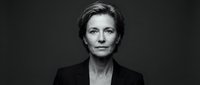 Mature woman with short gray hair wearing black blazer against dark background, professional headshot for corporate business portraits.