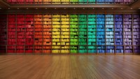 Rainbow colored library bookshelf wall with books arranged by color spectrum from red to violet creating vibrant gradient pattern in modern interior space.