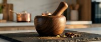 Wooden mortar and pestle with spices on slate board in modern kitchen setting for cooking and food preparation.