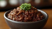 Homemade spicy beef chili con carne served in rustic black ceramic bowl, garnished with fresh parsley. Rich, hearty meat sauce with traditional Mexican seasonings.