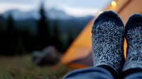 Cozy wool socks at sunset inside camping tent with mountain view and full moon. Relaxing outdoor lifestyle moment capturing warmth and adventure spirit.